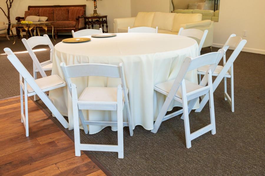 A round banquet table set with white padded folding chairs.